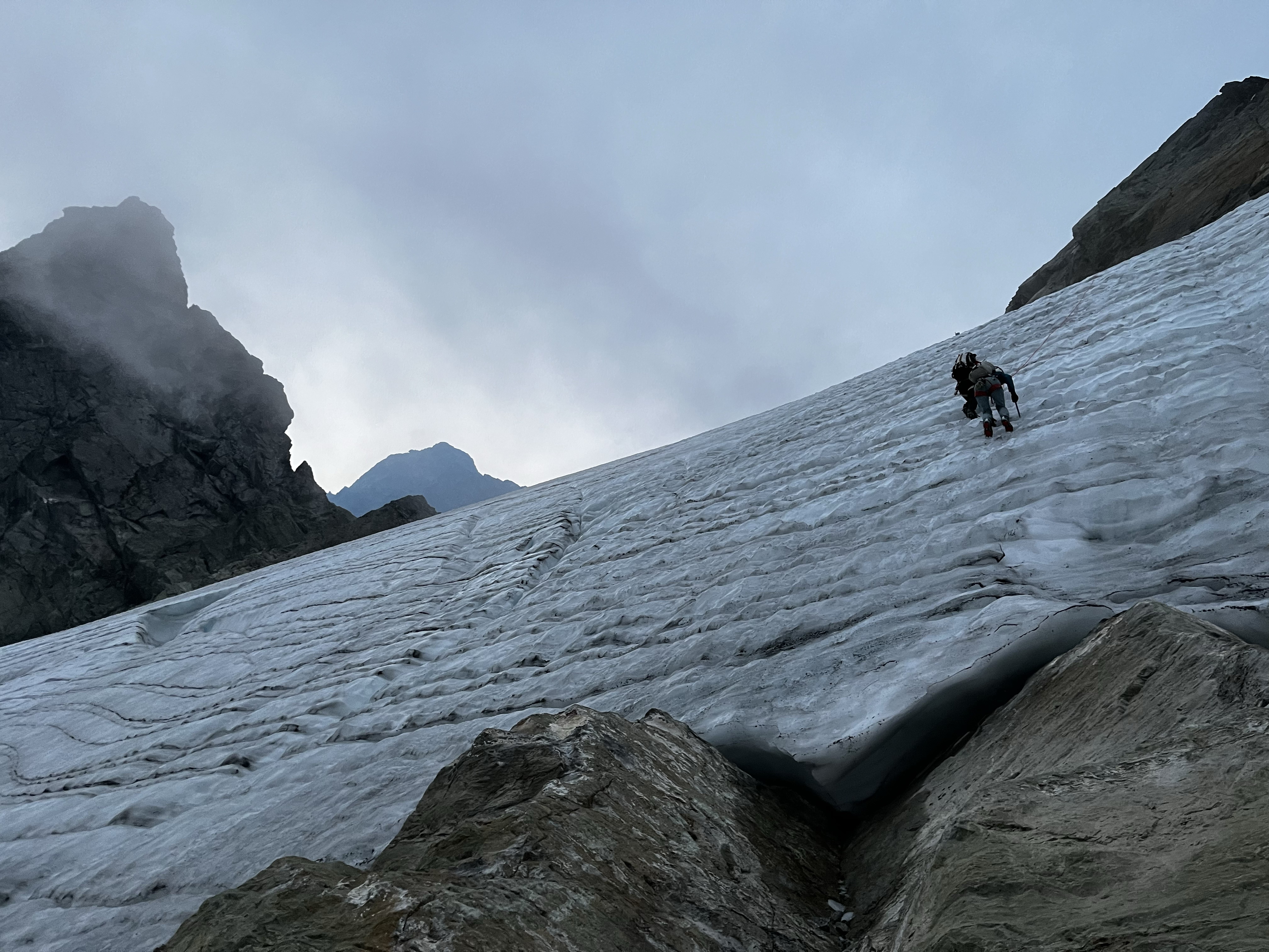 Two figures climbing low-angle glacier ice, pictured from below (butt shot).