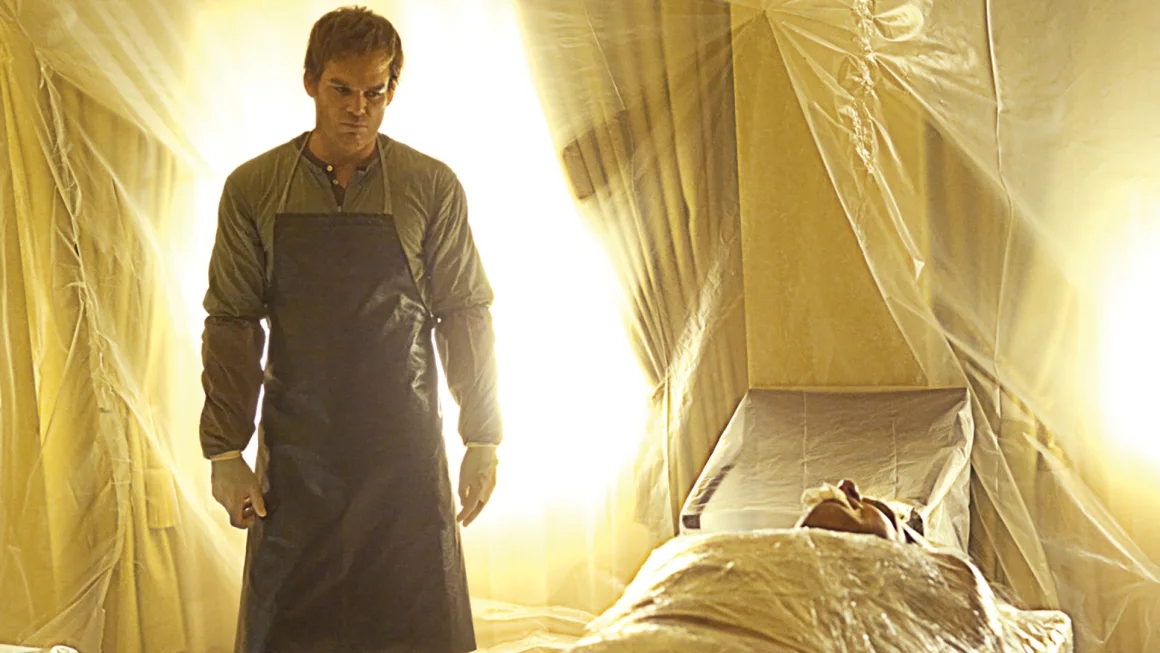 A still image of Dexter Morgan from the Shotime TV Series "Dexter". Dexter stands in his "kill room", covered in latex sheets with a victim bound on the table in front of him. Dexter wears a heavy-duty butcher's apron and surgical gloves, which appear similar to the Showa ice climbing gloves discussed in this article.